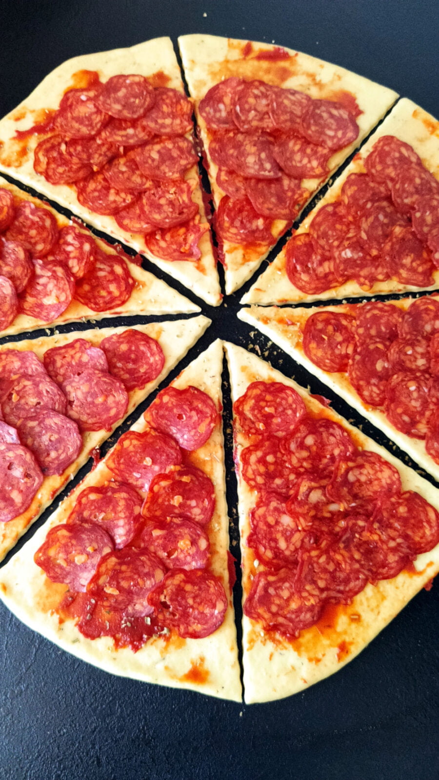 Plasterki pepperoni ułożone na cieście drożdżowym.