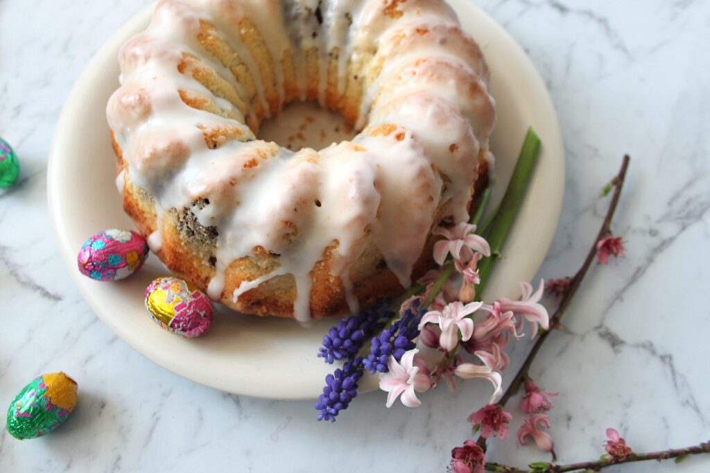 Babka wielkanocna z lukrem na białym talerzu, obok leżą pisanki