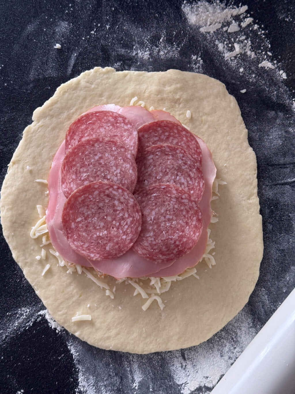 Nakładanie szynki, salami i tartej mozzarelli na ziemniaczany placek