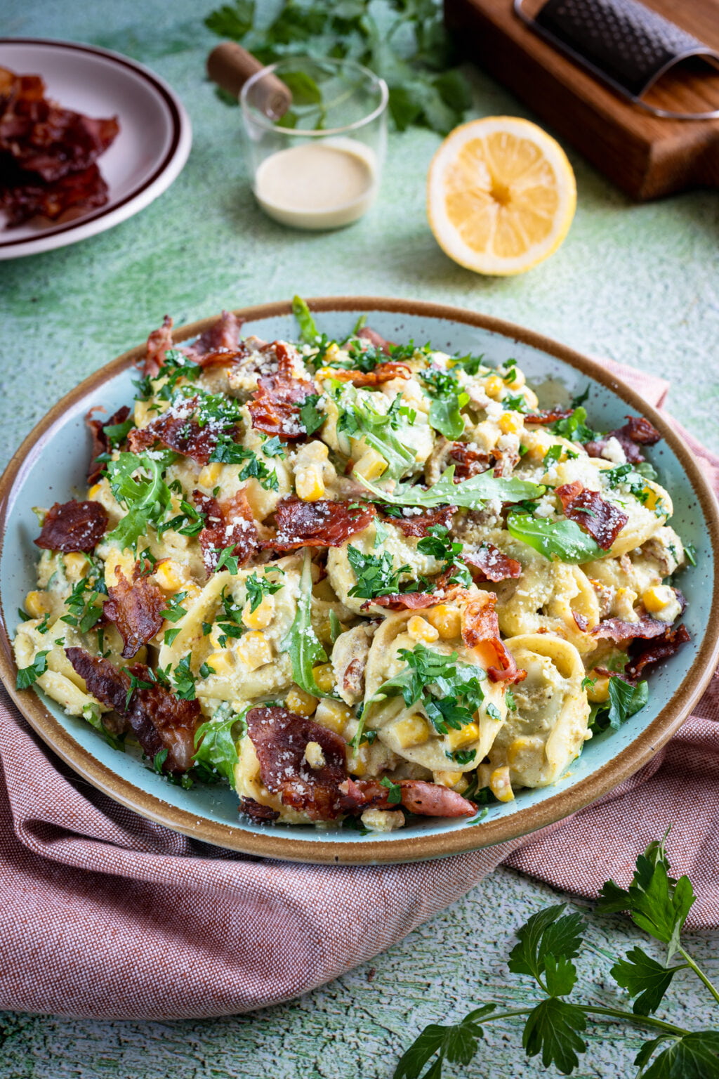 Sałatka z tortellini, boczkiem, suszonymi pomidorami i pesto w misce, posypana parmezanem i natką pietruszki