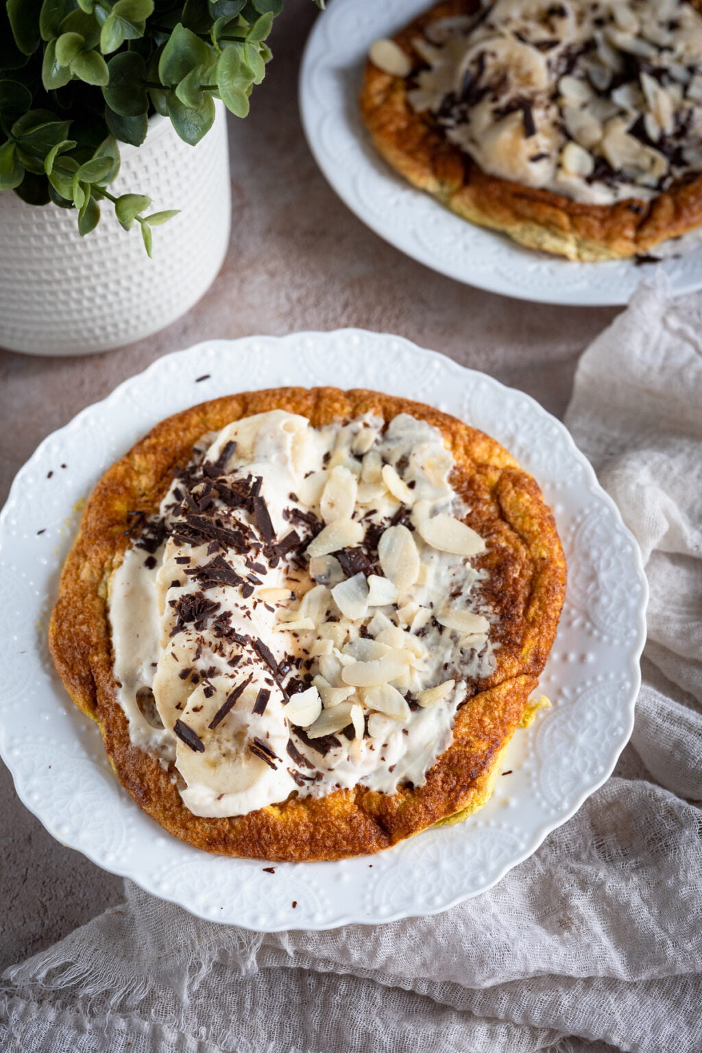 Puszysty omlet bananowy z kremem z jogurtu i masła orzechowego, plasterkami banana, gorzką czekoladą i migdałami.